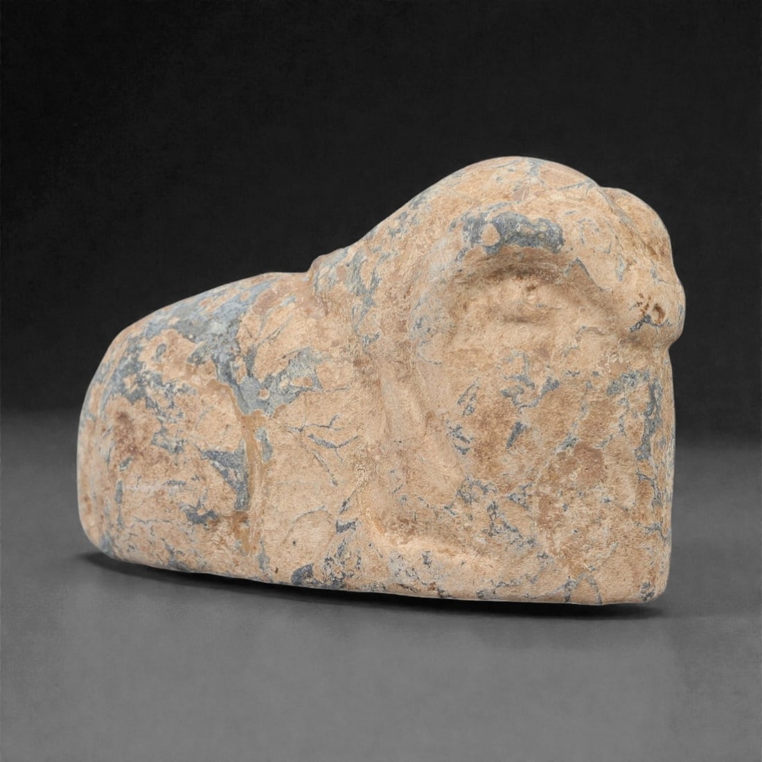 A Near Eastern Stone Ram Effigy, 3rd-2nd Millennium BCE, 97FL: Carved from light beige stone with natural blue-grey veining and surface patination, the object is formed as a stylized ram in a recumbent pose. The head is rendered in low relief with simplified faci