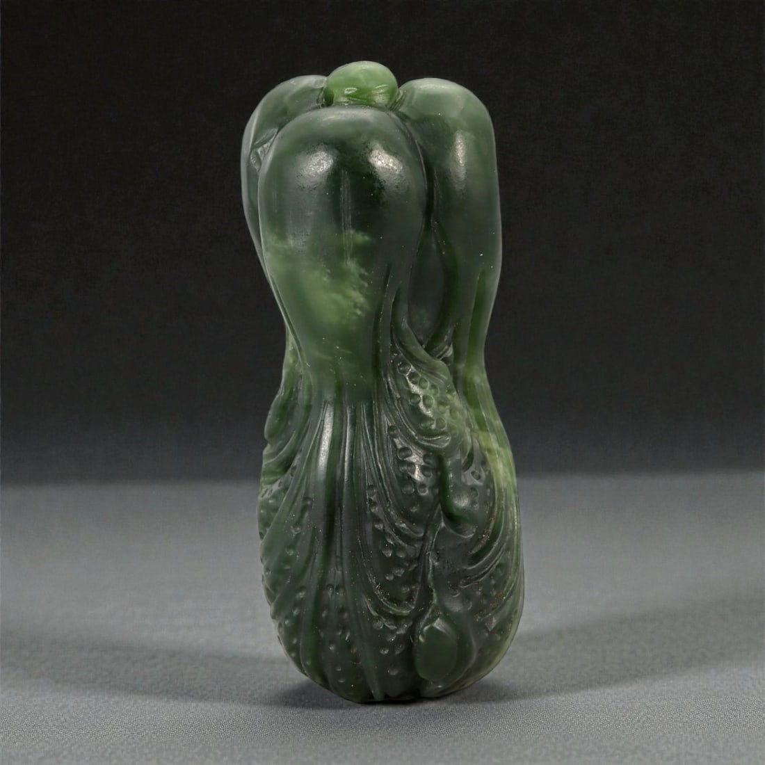 A Chinese Jade Cabbage Carving, 20th Century, 37FA: Carved from dark green jade with lighter mottled inclusions and areas of subtle translucency, the object represents a stylized cabbage rendered in the round. The vegetable is depicted upright, with ov