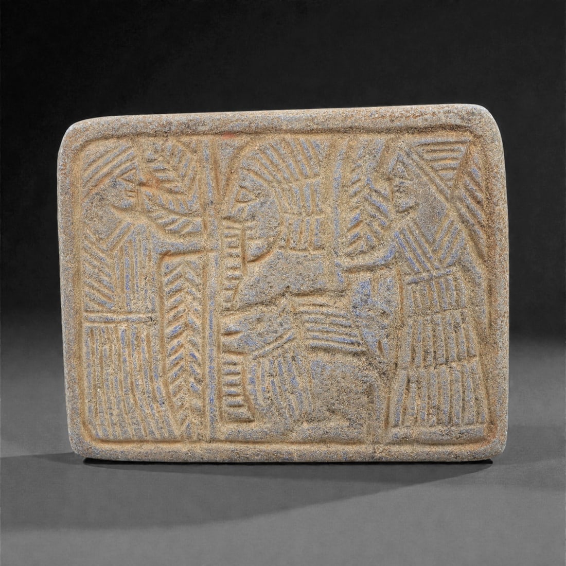 An Ancient Near Eastern Lapis Lazuli Relief Plaque, 2nd-1st Millennium BCE, 84FM: Carved from lapis lazuli with natural blue-grey veining and surface patination, the rectangular plaque is divided into three vertical panels. The left panel depicts a standing figure with a stylized h