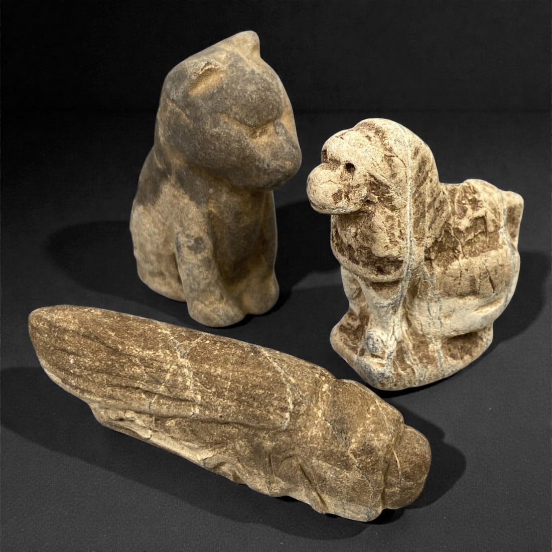 A Group of Three Near Eastern Stone Zoomorphic Carvings, 2nd-1st Millennium BCE, 69FM: Comprising three stone zoomorphic carvings, each formed from light brown to grey stone with visible surface fissures and tonal variation. The left carving depicts a stylized quadruped, likely a bear o