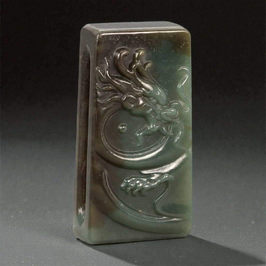 A Chinese Nephrite Jade Belt Buckle, 20th Century, 50FA: Carved from dark green nephrite jade with areas of mottled brown and olive tonal variation, the buckle is rectangular in form with slightly rounded edges and a flat reverse. The obverse is carved in l