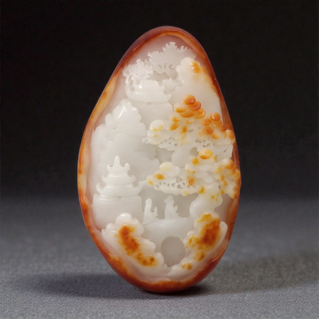 A Chinese Hetian Nephrite Jade Landscape Plaque, Qing Dynasty, 20th Century, 38YB: Carved from pale white Hetian nephrite with areas of warm russet skin retained along the outer edge, the plaque is worked in an elongated oval form with rounded contours. One face is carved in low rel
