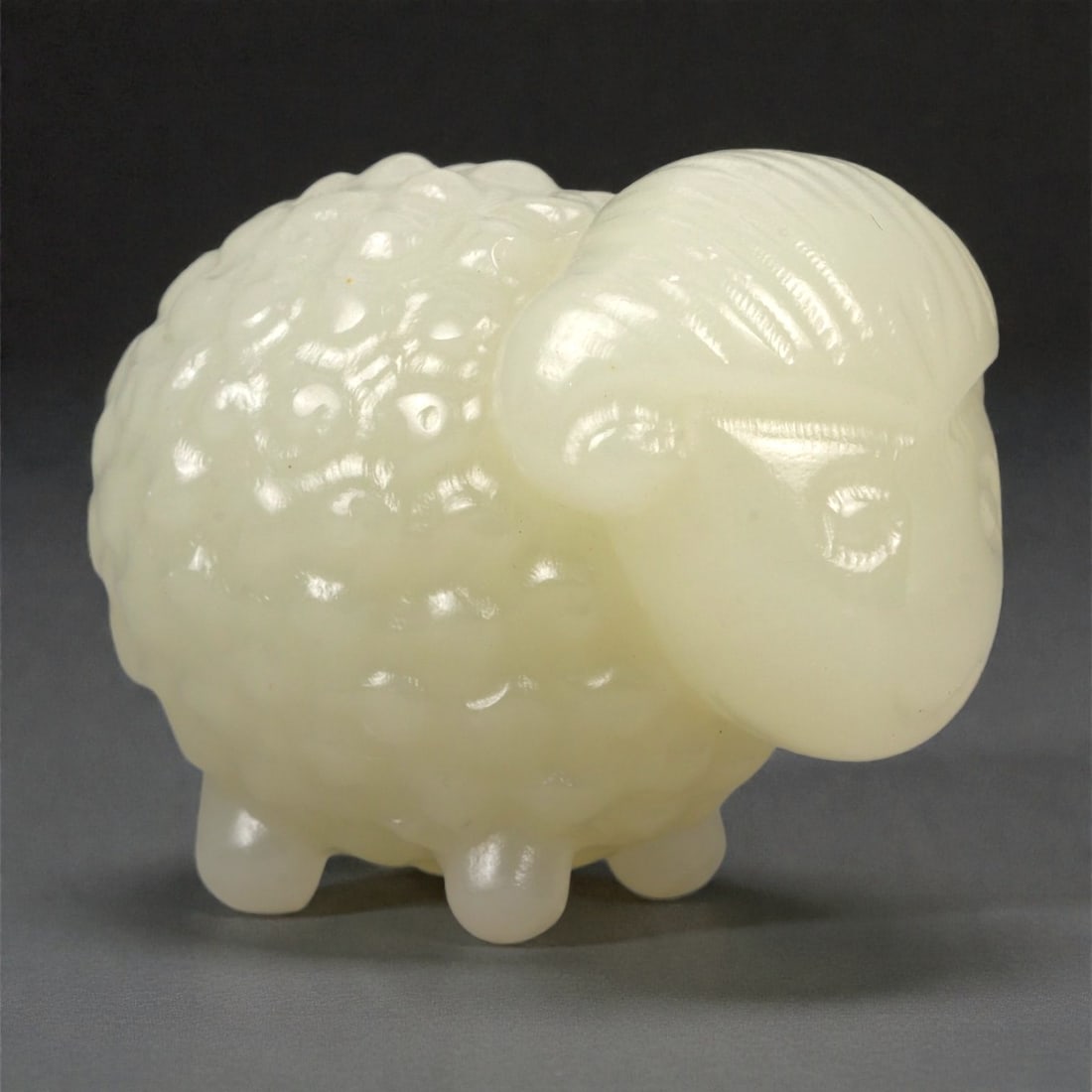 A Chinese Nephrite Jade Ram Figure, 20th Century, 90FA: Carved from pale celadon nephrite jade with a soft, semi-translucent appearance and subtle tonal variation, the figure represents a ram shown standing in a compact, rounded posture. The body is modele