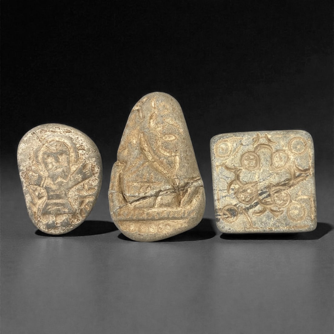 A Group of Three Christian Period Stone Carving Reliefs, 4th-7th Century, 60FM: Comprising three stone carving reliefs, each formed from naturally shaped or cut stone with visible surface fissures and tonal variation. The leftmost oval relief depicts a haloed figure with outstret