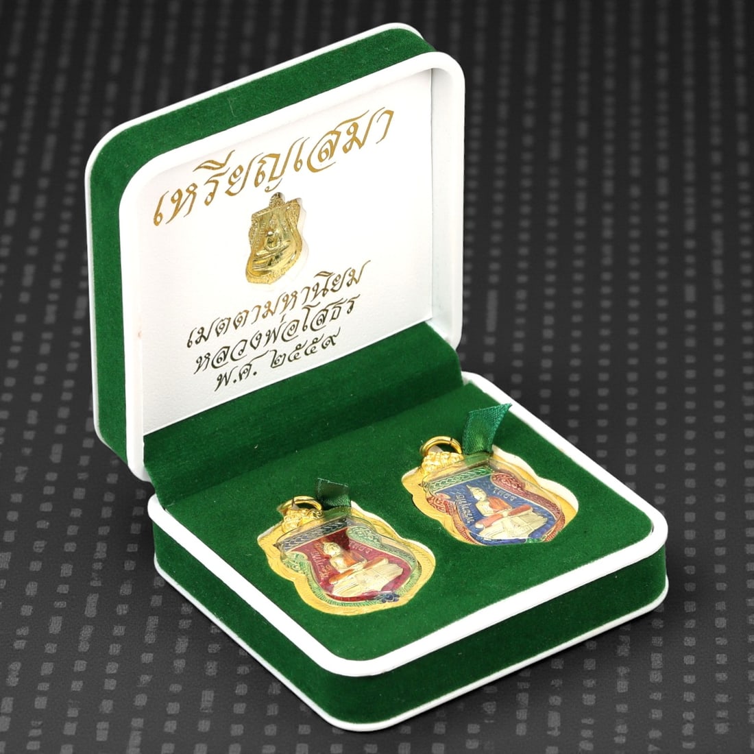 A Thai Enamel and Gilt Bronze Seated Monk Amulet Set, Late 20th Century, 53FJ: The set comprises two shield-shaped amulets cast in bronze and finished with gilt frames and polychrome enamel, each depicting a seated Buddhist monk shown frontally in meditative posture. The figure