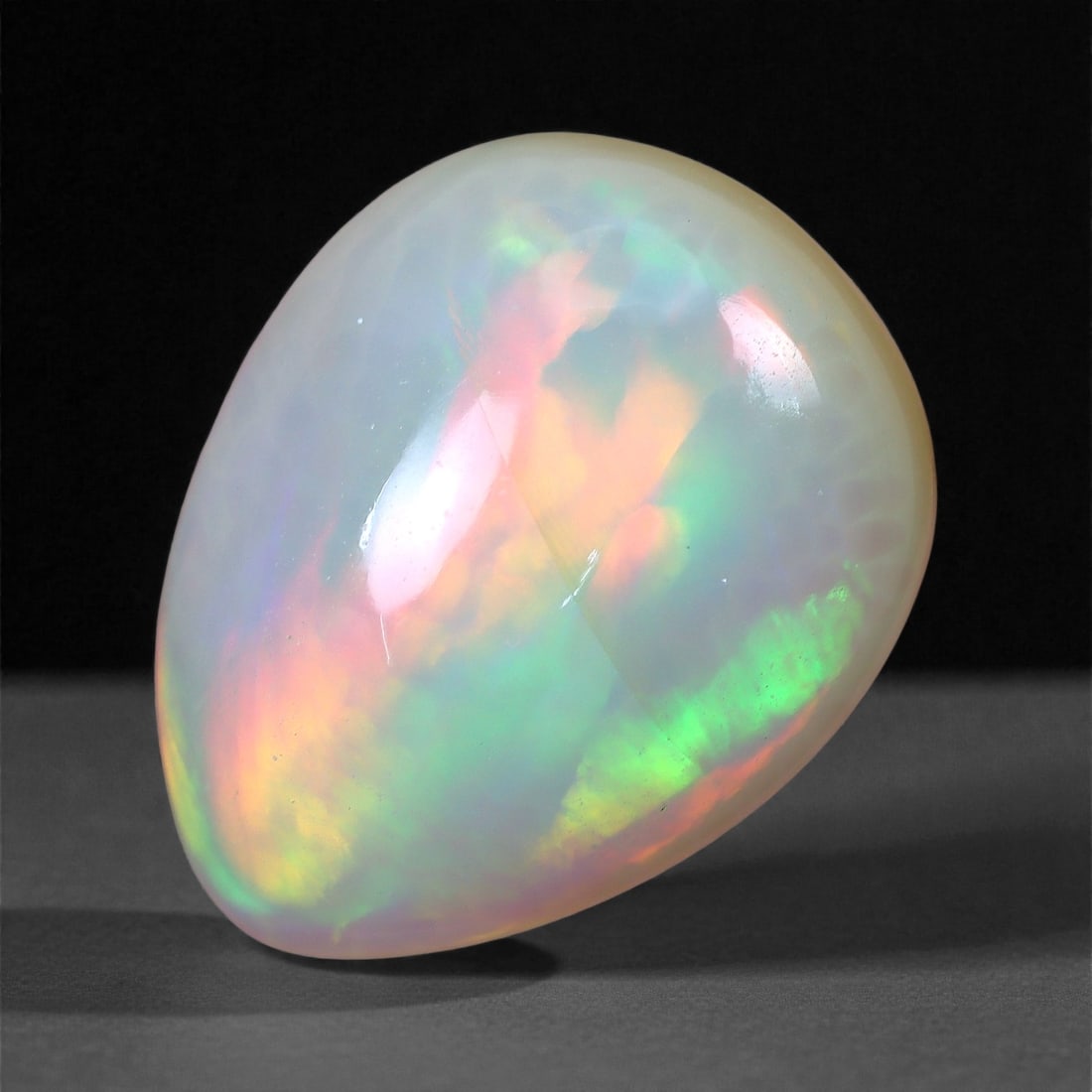 5.23 Carats Sunset Prism Welo Opal - Natural Ethiopian Gemstone 13.7x10.7x7.3mm, 12XH: This vibrant Welo opal showcases a striking prism of color, with fiery bands of orange, lime green, and vivid magenta surging through its translucent body. The broad flashes seem to radiate outward li