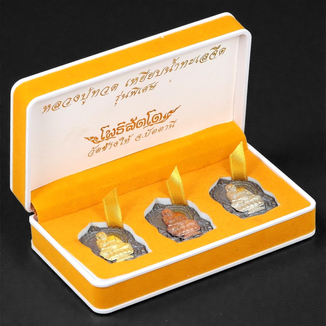 A Thai Bronze Seated Monk Amulet Set, Late 20th Century, 26FJ: The set comprises three small rectangular amulets cast in bronze, each depicting a seated Buddhist monk shown frontally in meditative posture. The figure is rendered in low to moderate relief, with si