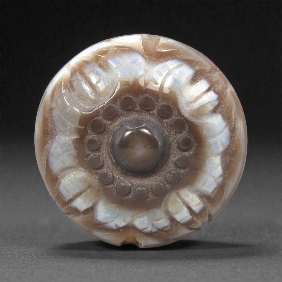 A Chinese Agate Bead, 20th Century, 45FK: Carved from banded agate with translucent brown and milky white tonal variations, the bead is circular in form with a flattened profile. The surface is worked in relief with a concentric design, compr