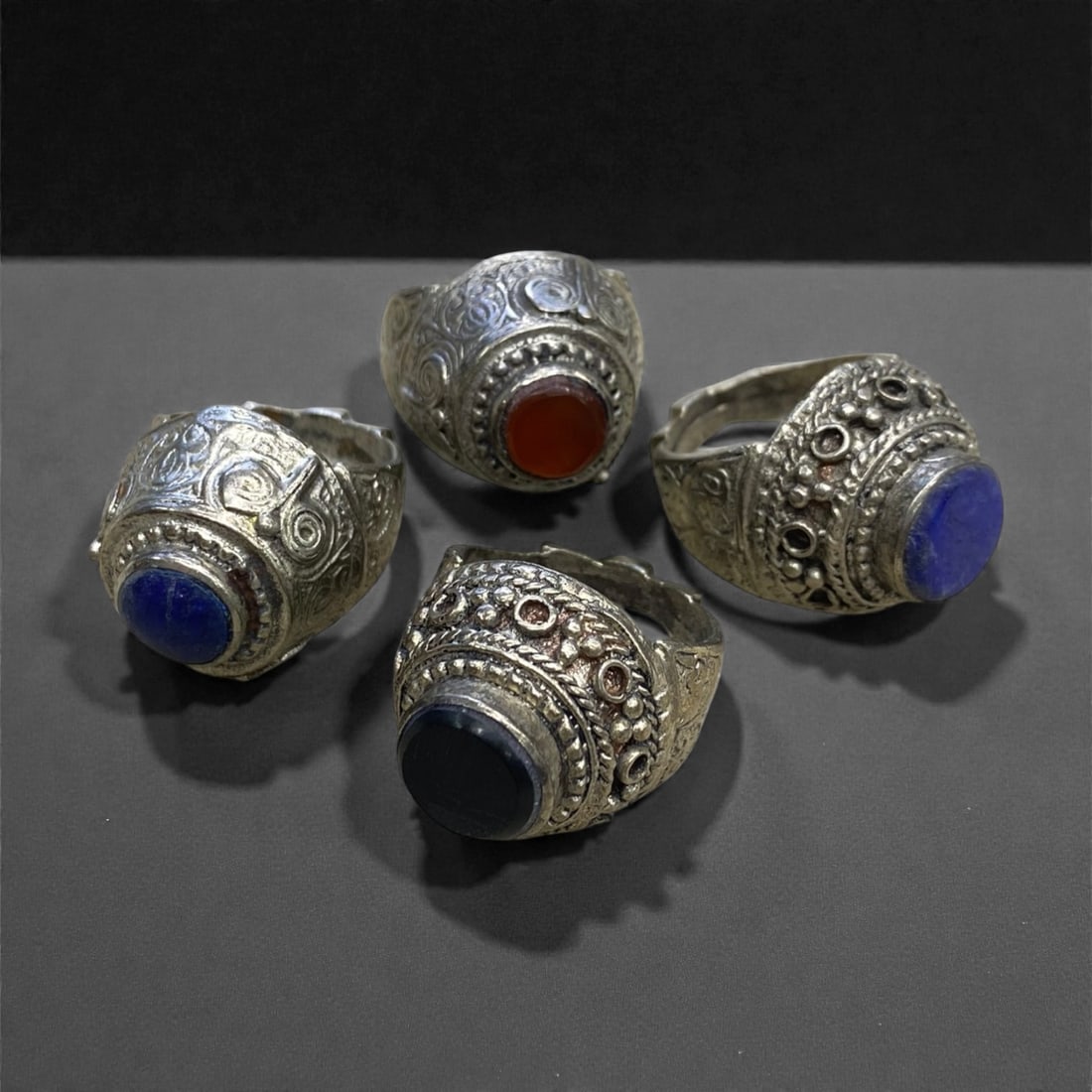 A Group of Four Antique Silvered Bronze Rings, 19th Century, Size 8-8.5US, 60g, 67AA: Each ring is crafted from silvered bronze, featuring ornate metalwork including filigree, repousse, and granulation details. The bezels are set with composite stones, the surfaces exhibit minor patina