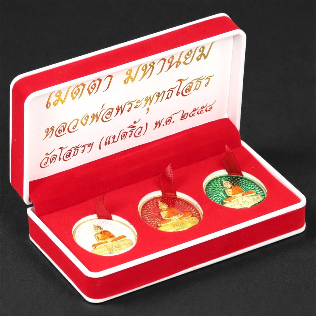 A Thai Enamel and Gilt Bronze Seated Monk Amulet Set, Late 20th Century, 55FJ: The set comprises three circular amulets cast in bronze and finished with gilt and polychrome enamel, each depicting a seated Buddhist monk shown frontally in meditative posture. The figure is rendere