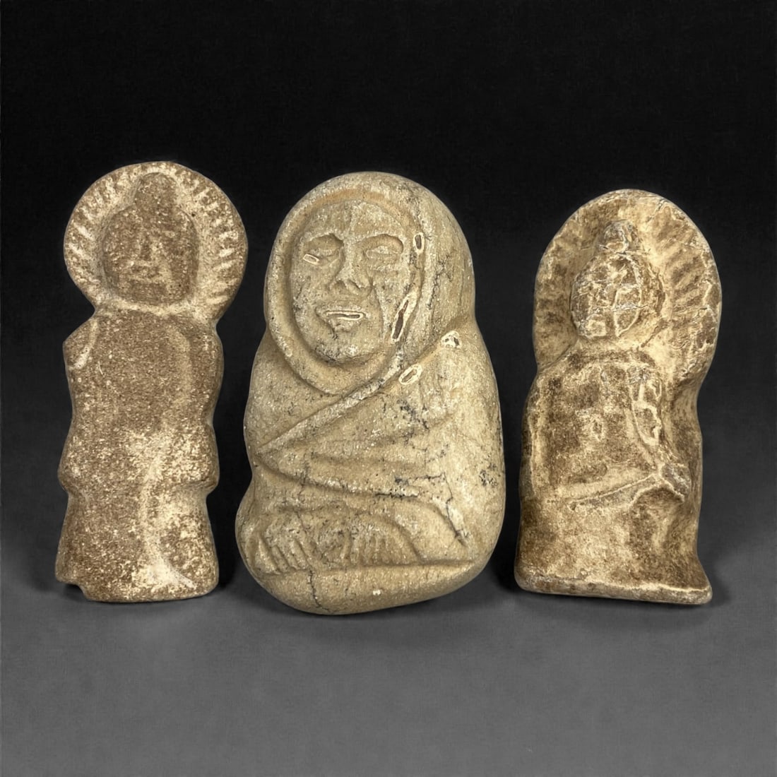 A Group of Three Edo Period Buddhist Stone Carvings, 17th-19th Century, 23FN: Carved from stone with natural tonal variation, surface wear, and mineral encrustation, the three objects depict Buddhist figures in low to medium relief. The leftmost figure is rendered in a standing