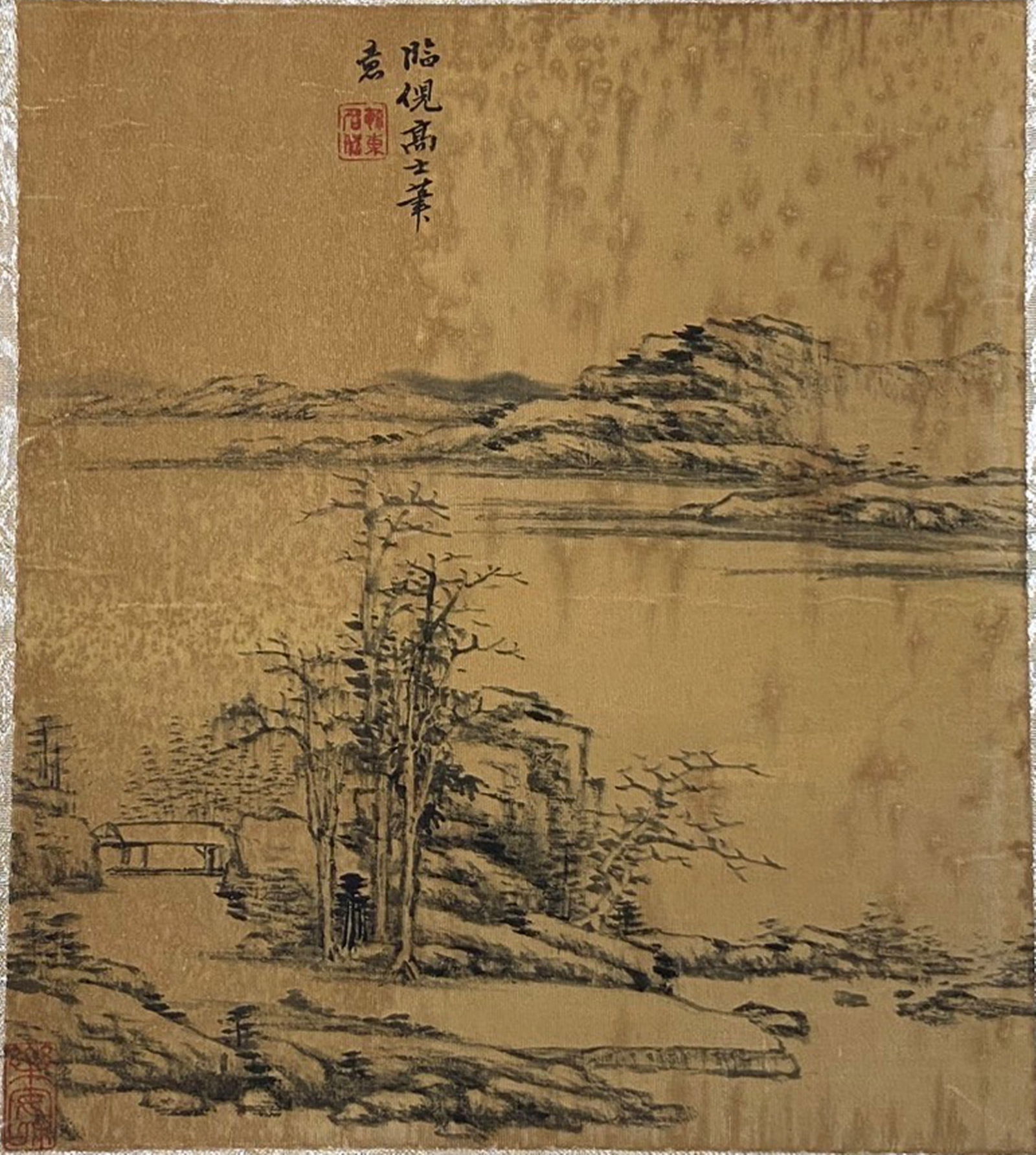 A Chinese Ink and Color Textile Print, After Ni Zan's 'Wintry Trees by a Lake', 20th Century, 40FK: Printed on woven silk or hemp textile with a gold-toned ground, the composition follows the sparse, reductive style of Yuan Dynasty painter Ni Zan. Bare, angular trees stand beside a quiet lake, with
