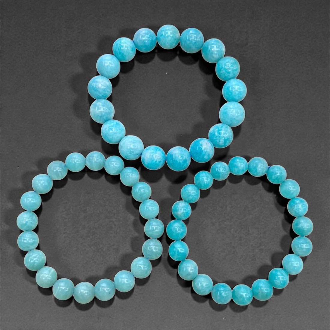 A Group of Three Aquamarine Beaded Bracelets, 94g, 73AA: Each bracelet is composed of polished round aquamarine beads, displaying a soft, translucent blue hue with subtle tonal variations and natural mineral inclusions. The beads are strung on elastic cord