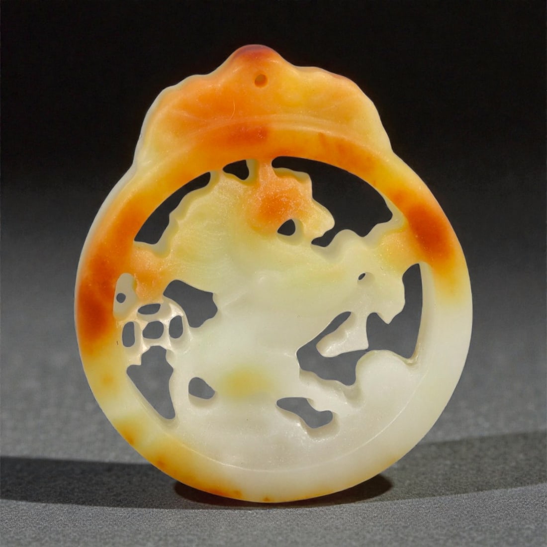 A Chinese Nephrite Jade Openwork Pendant, 20th Century, 63FA: Carved from pale cream nephrite jade with pronounced russet inclusions, the pendant is worked in openwork and low relief with a circular form surmounted by a scalloped upper edge. The composition feat
