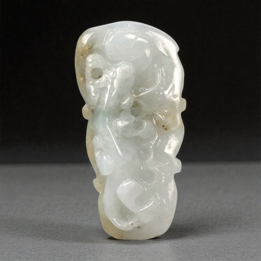 A Chinese Jadeite Jade Mythical Beast Carving, 20th Century, 59FA: Carved from pale jadeite jade with a milky white to faint celadon tone and areas of natural clouding, the carving represents a stylized mythical beast rendered in high relief. The creature is shown in