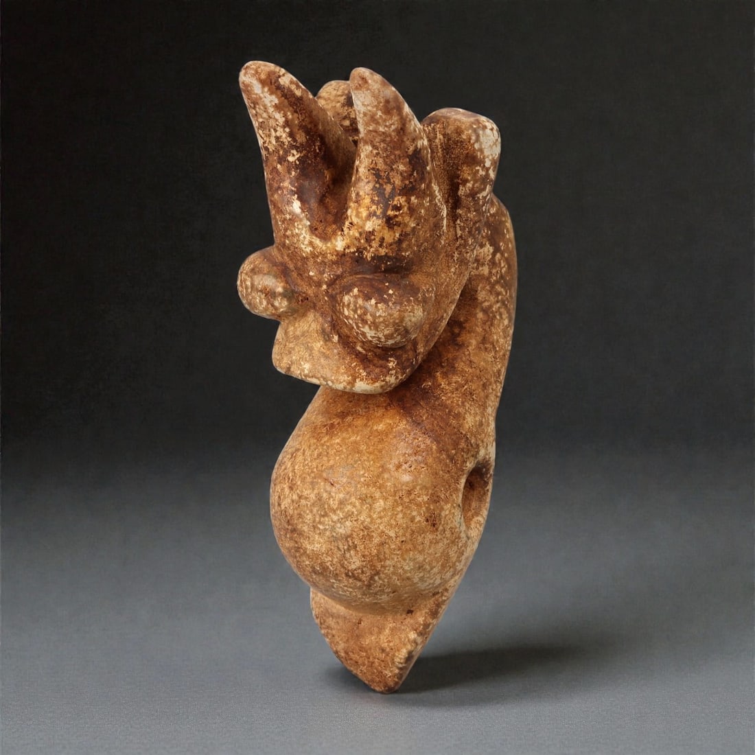 A Chinese Hardstone Zoomorphic Pendant, 20th Century, 36YB: Carved from mottled brown hardstone with lighter inclusions and an uneven, granular surface texture, the object takes the form of a highly stylized zoomorphic figure rendered in the round. The upper s