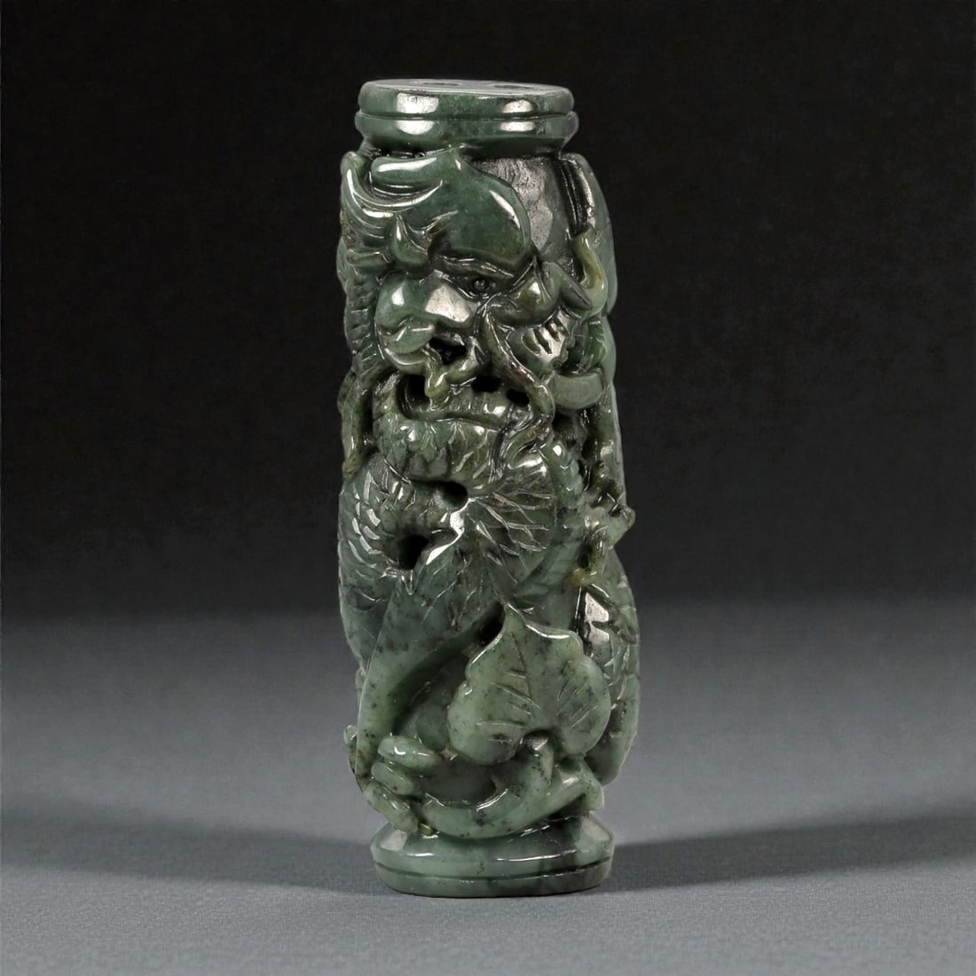 A Chinese Jadeite Carved Cylindrical Pendant, 20th Century, 67FB: Carved from dark green jadeite with lighter mottling and areas of natural translucency, the object is formed as a vertical cylindrical pendant with flat upper and lower terminals. The exterior is work