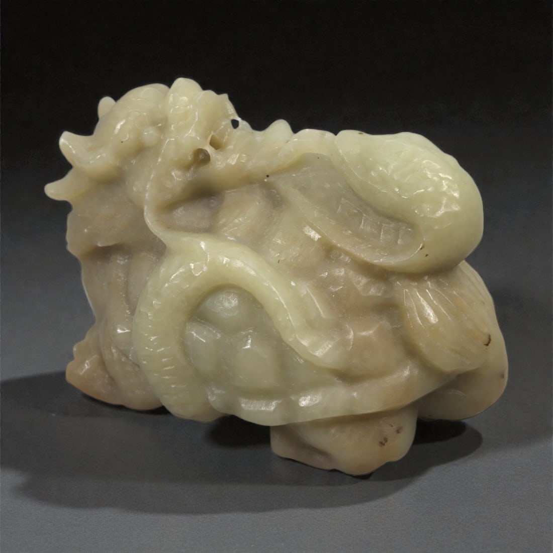 A Chinese Nephrite Jade Dragon and Snake Group, 20th Century, 92FB: Carved from pale celadon Hetian nephrite jade with areas of milky translucency and minor natural inclusions, the sculpture is worked in the form of a crouching dragon entwined with a snake. The dragon