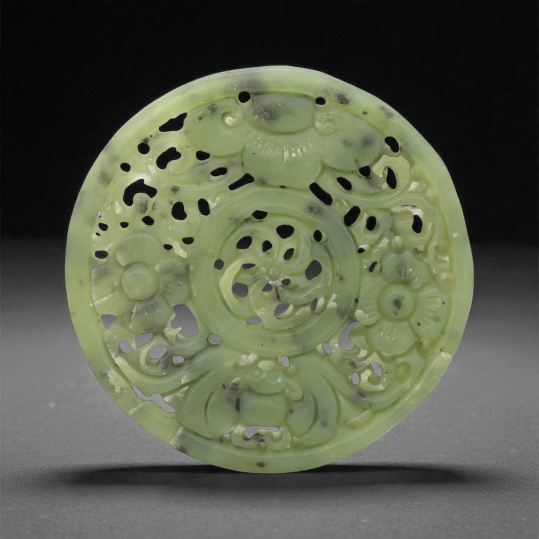 A Chinese Hetian Jade Openwork Plaque, 20th Century, 85FH: Carved from pale green Hetian jade with darker speckled inclusions, the plaque is circular in form and worked in openwork relief. The design is organized around a central roundel, pierced and carved w