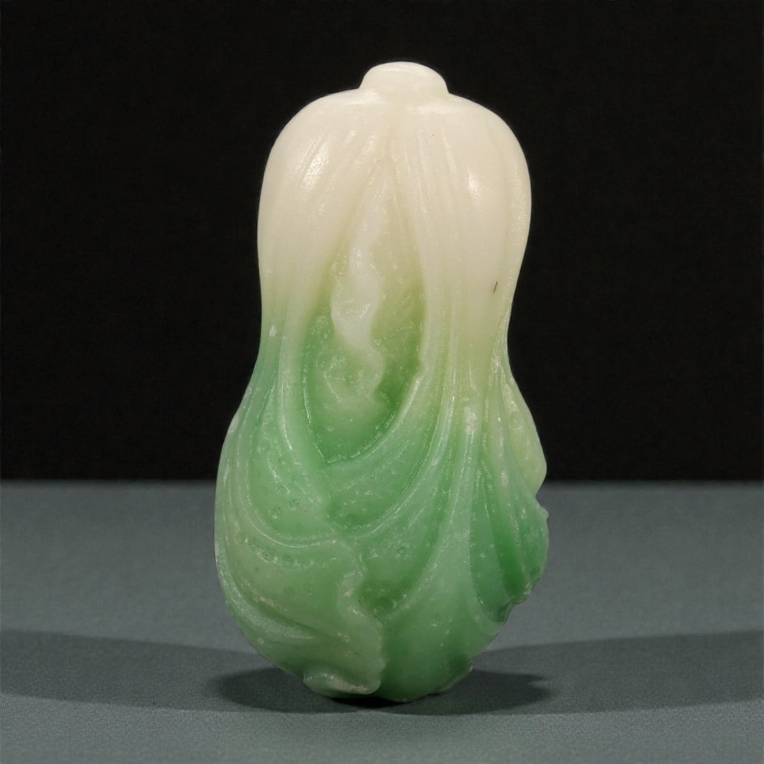 A Chinese Jadeite Jade Cabbage-Form Carving, 20th Century, 62FB: Carved from jadeite jade with a creamy white upper section graduating naturally into vivid apple-green tones toward the base, the carving is modeled in the form of a leafy cabbage. The gently flaring