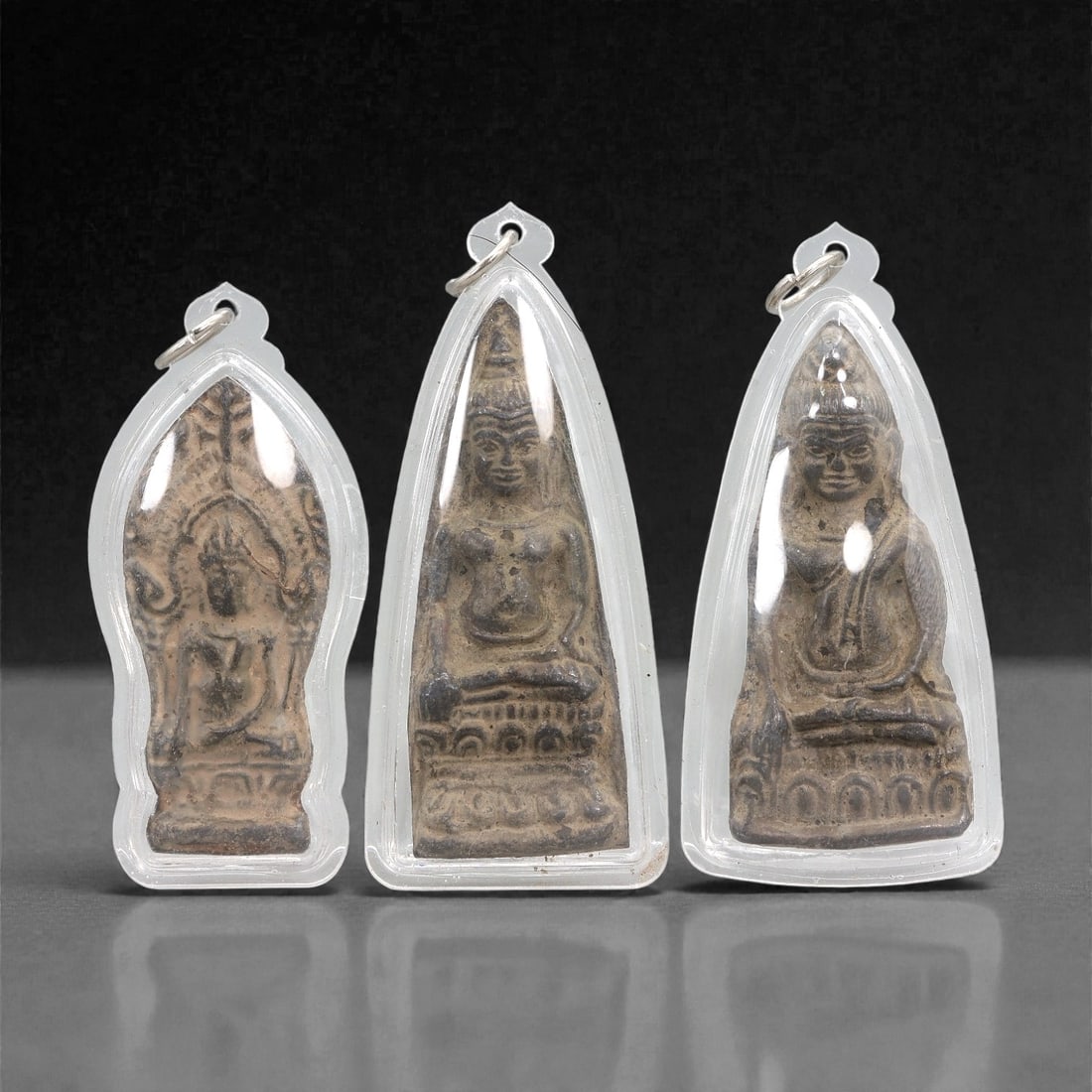 A Group of Three Bronze Buddhist Amulets in Acrylic Cases, 20th Century, 24FJ: The group comprises three small Buddhist amulets cast in bronze and enclosed within clear molded acrylic pendant cases fitted with metal suspension rings. Each amulet is vertically oriented and depict