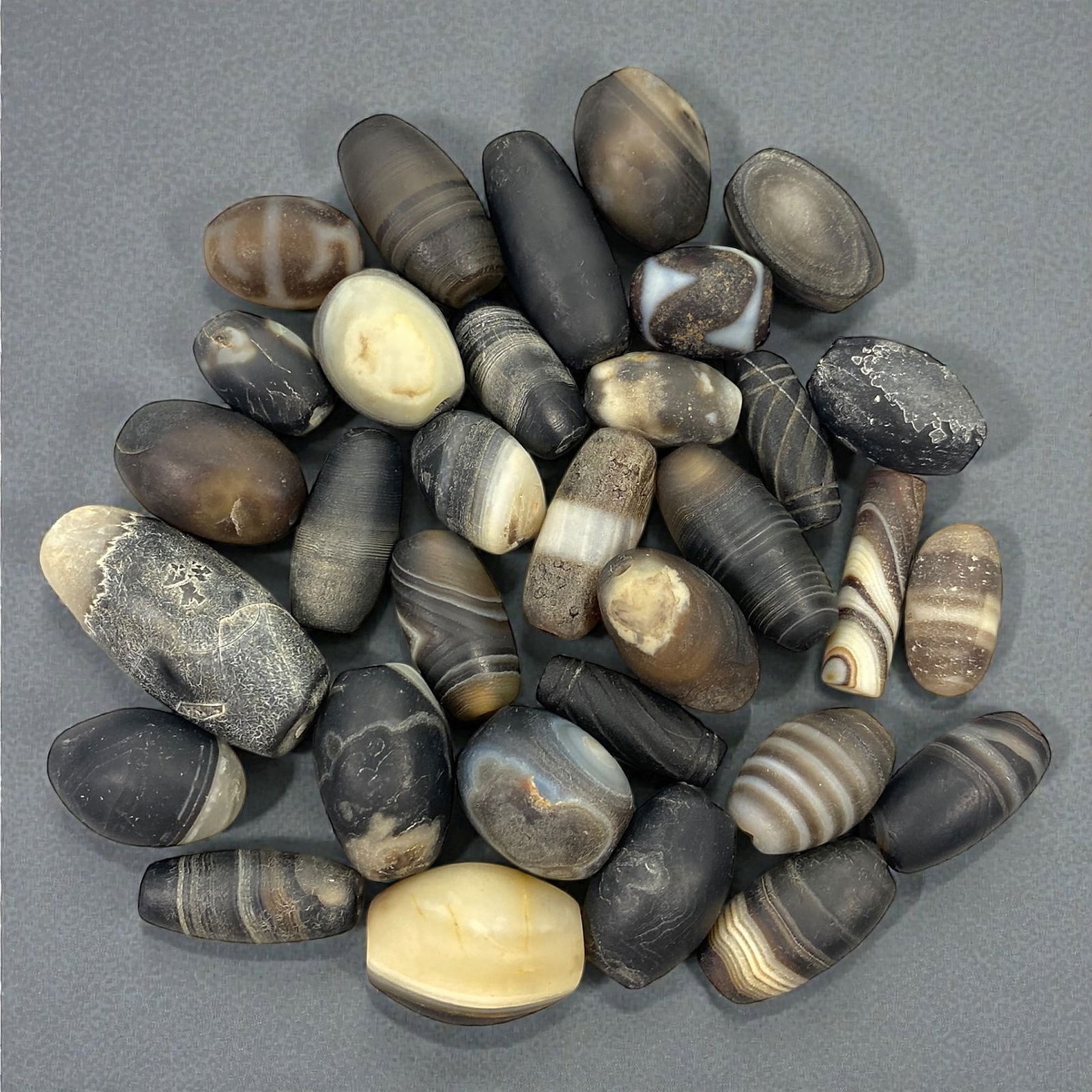 A Group of Himalayan Agate Beads, Medieval Period, 87V: Comprising a group of elongated, barrel-shaped, and ovoid beads carved from banded agate, the assemblage displays a range of natural striations, concentric banding, and eye-like formations in tones of