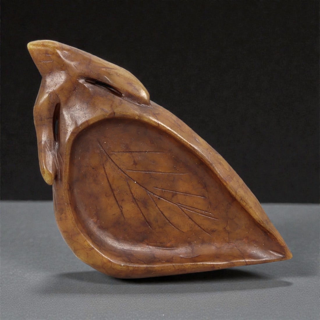 A Chinese Hardstone Brush Rest Dish, 20th Century, 93FC: Carved from warm brown hardstone with subtle tonal variation and fine natural fissures, the object is worked as a shallow dish intended for use in the scholar's studio. The form is modeled as a styliz