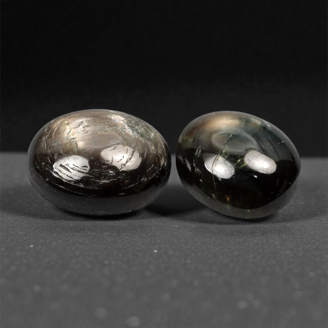 4.69 Carats Dark Greyish Green Star Sapphire Parcel - Natural Sri Lankan Stones, 370A: This exceptional parcel of two loose star sapphires captivates with their deep, moody greyish-green hues and the subtle, luminous asterism that emerges under direct light. The smooth, cabochon-cut sur