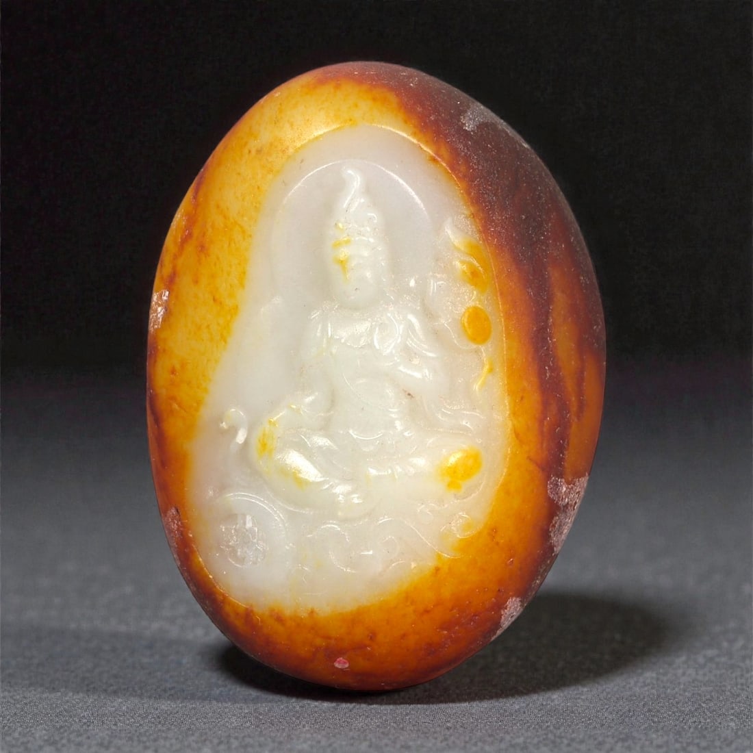 A Chinese Jade Buddha Plaque, 20th Century, 54FB: Carved from bi-colored jade with a creamy white interior and a surrounding russet-brown skin, the plaque is oval in form and worked in shallow relief. One face depicts a seated Buddha shown frontally,