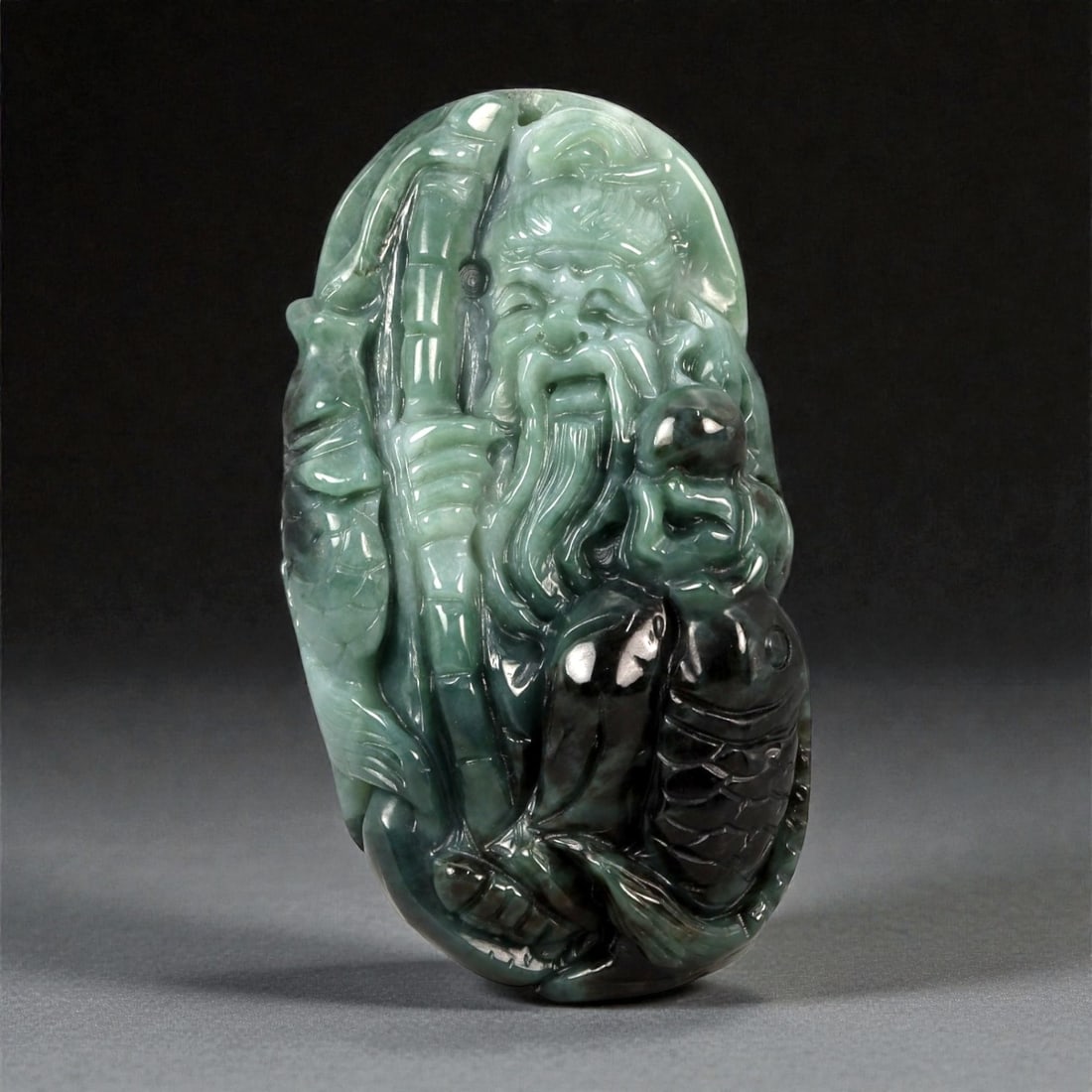 A Chinese Jadeite Jade Figure of Shoulao, 20th Century, 46FB: Carved from dark green jadeite with areas of lighter translucency and natural tonal variation, the figure represents Shoulao, the Daoist god of longevity, shown standing and holding a staff and a gour