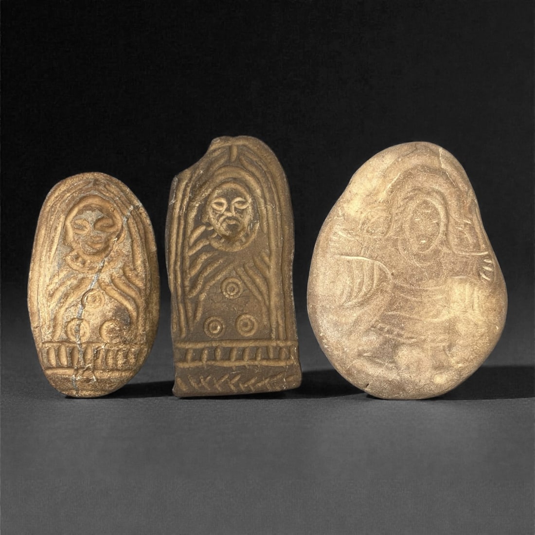 A Group of Three Christian Period Stone Carving Reliefs, 4th-7th Century, 66FM: Comprising three stone carving reliefs, each formed from naturally shaped or cut stone with visible surface fissures and tonal variation. The leftmost oval relief depicts a haloed figure with incised