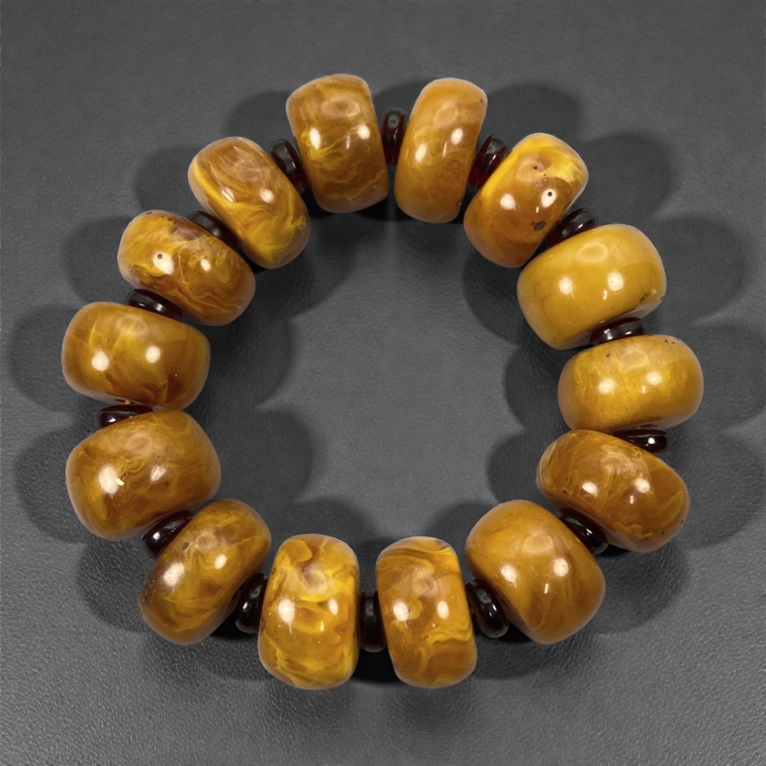A Chinese Amber Beaded Bracelet, 20th Century, 43FJ: The bracelet is composed of a continuous strand of large barrel-shaped beads carved from natural amber, each bead richly translucent and displaying swirling internal inclusions in warm tones ranging f