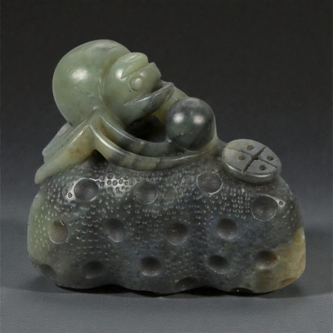 A Chinese Nephrite Jade Spider Carving, 20th Century, 78FB: Carved from dark green nephrite jade with mottled inclusions and areas of lighter translucency, the object is modeled as a spider resting upon a textured ground. The body is carved in the round, with