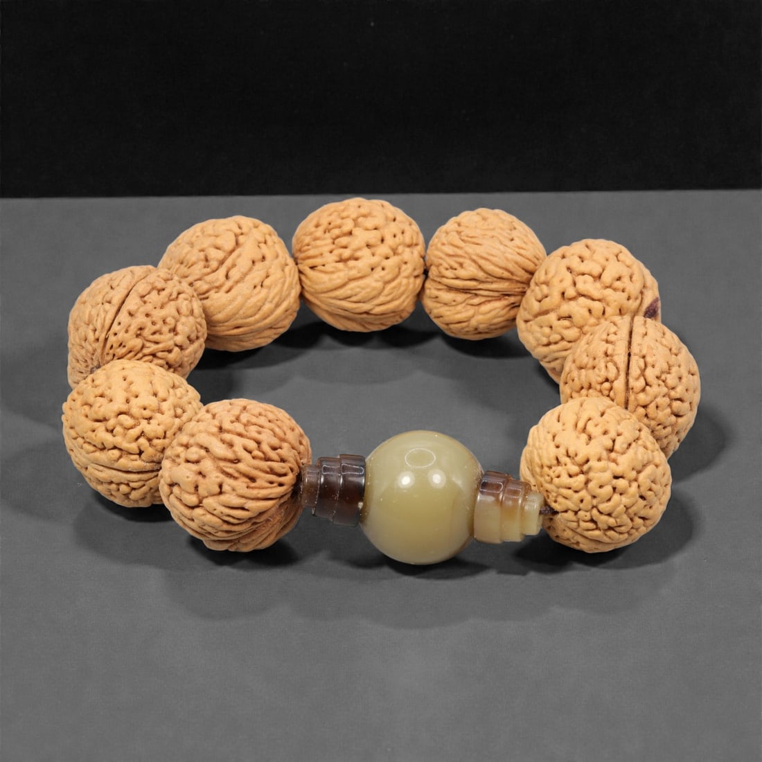 A Chinese Seed and Hetian Jade Bead Bracelet, 20th Century, 55YC: The bracelet is composed of a continuous strand of large natural seed beads, each approximately spherical with deeply textured surfaces and natural fissuring, strung to form a compact circular bracele