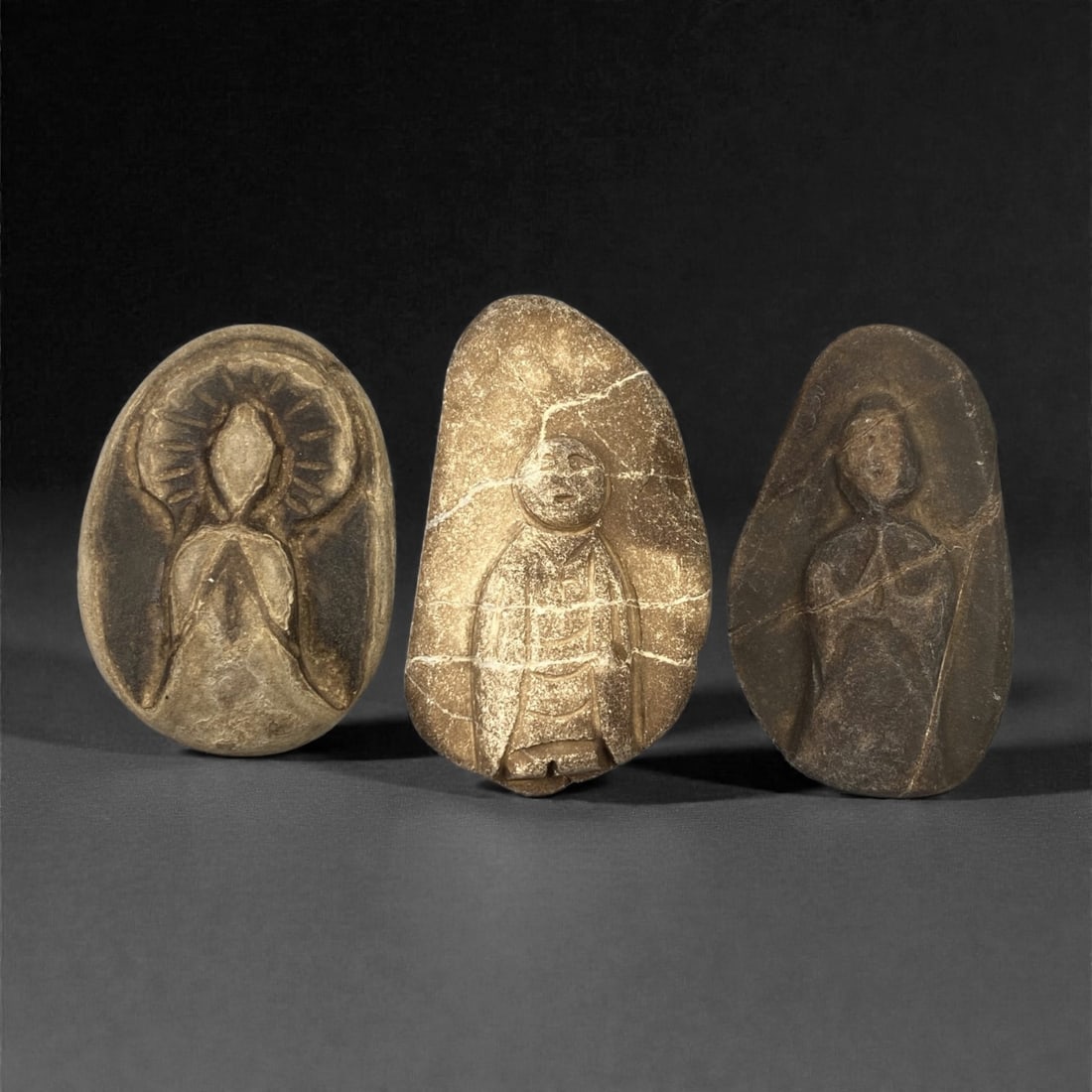A Group of Three Edo Period Buddhist Stone Carvings, 17th-19th Century, 97FM: Carved from stone with natural tonal variation, surface wear, and mineral encrustation, the three objects depict Buddhist figures in shallow relief, set within irregular stone matrices. The leftmost c