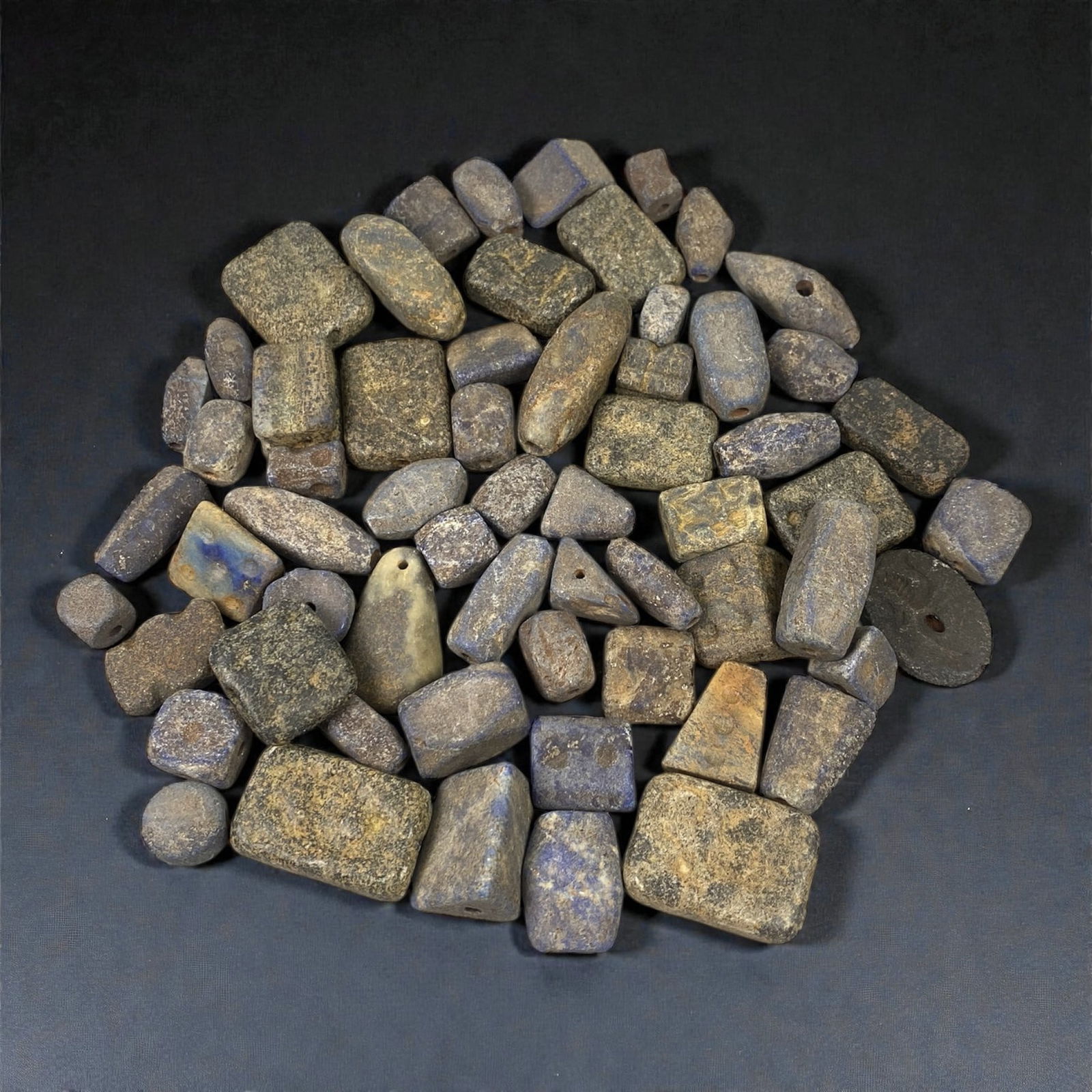 A Group of Mesopotamian Lapis Lazuli Beads, 3rd-2nd Millennium BCE, 33W: Comprising sixty-one beads carved from lapis lazuli of varied tonal quality, the group includes rectangular, barrel-shaped, cylindrical, discoid, and irregular geometric forms, each pierced longitudin