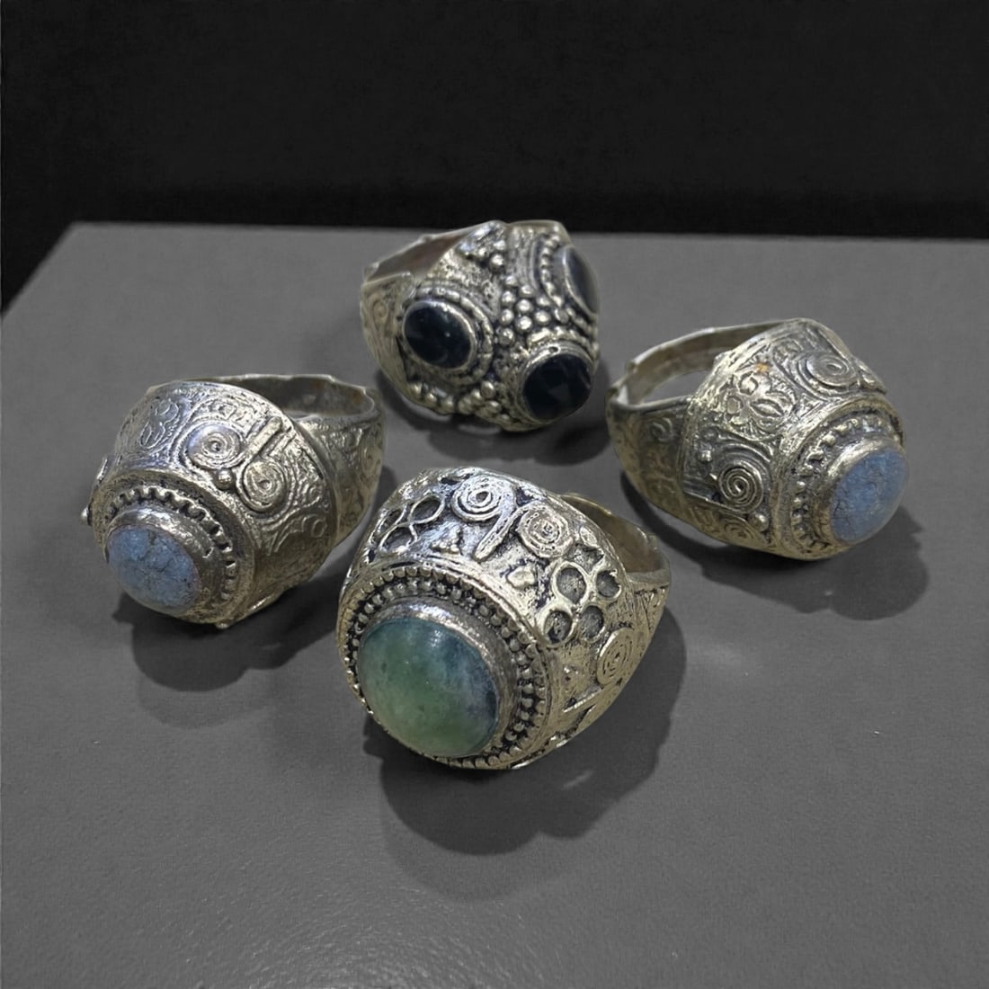 A Group of Four Antique Silvered Bronze Rings, 19th Century, Size 8US, 62g, 65AA: Each ring is crafted from silvered bronze, featuring ornate metalwork including filigree, repousse, and granulation details. The bezels are set with composite stones, the surfaces exhibit minor patina