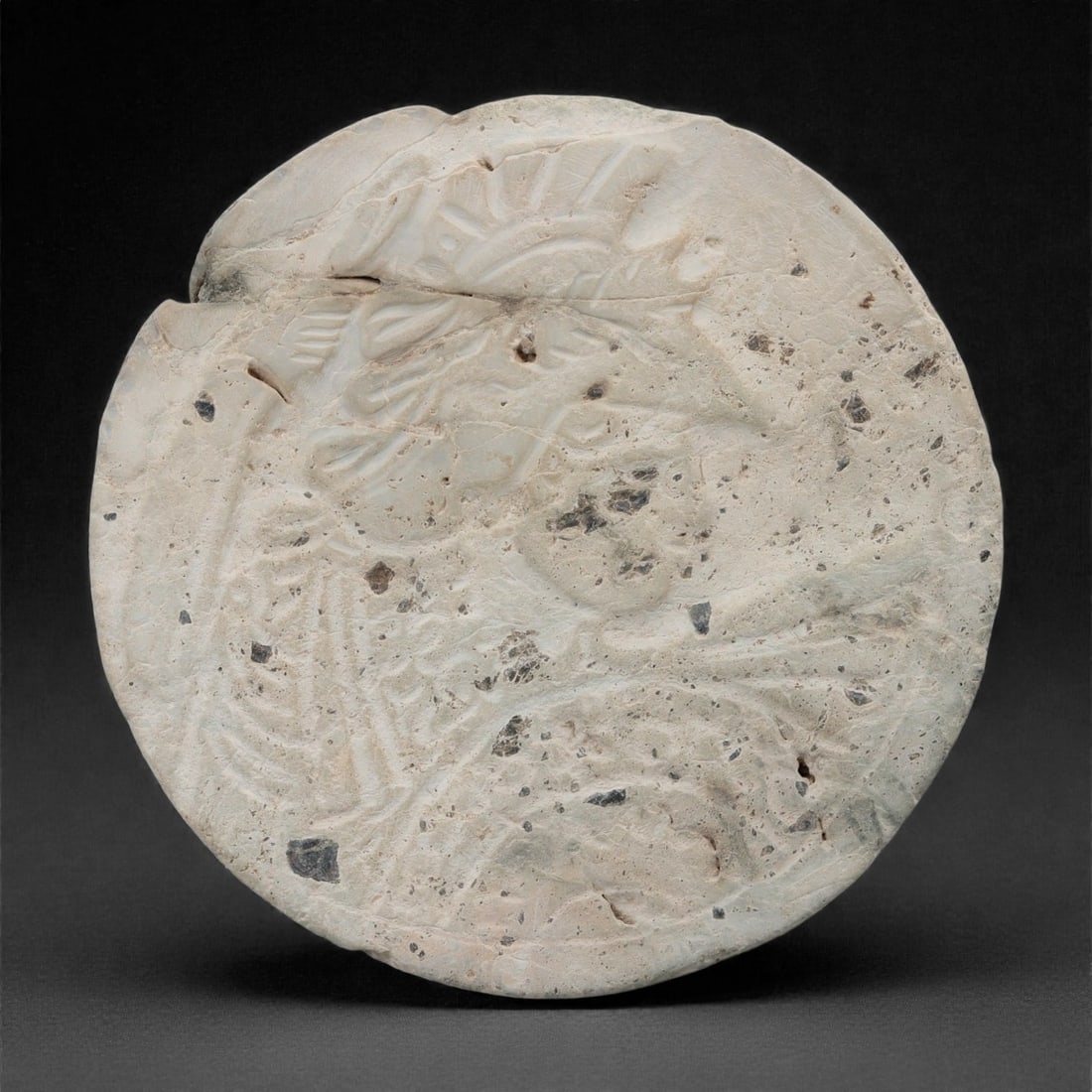 A Roman Stone Plaque, 1st-3rd Century CE, 59W: Carved from pale limestone with visible mineral inclusions and natural veining, the circular plaque is worked in low relief on one face. The surface is decorated with a continuous vegetal composition