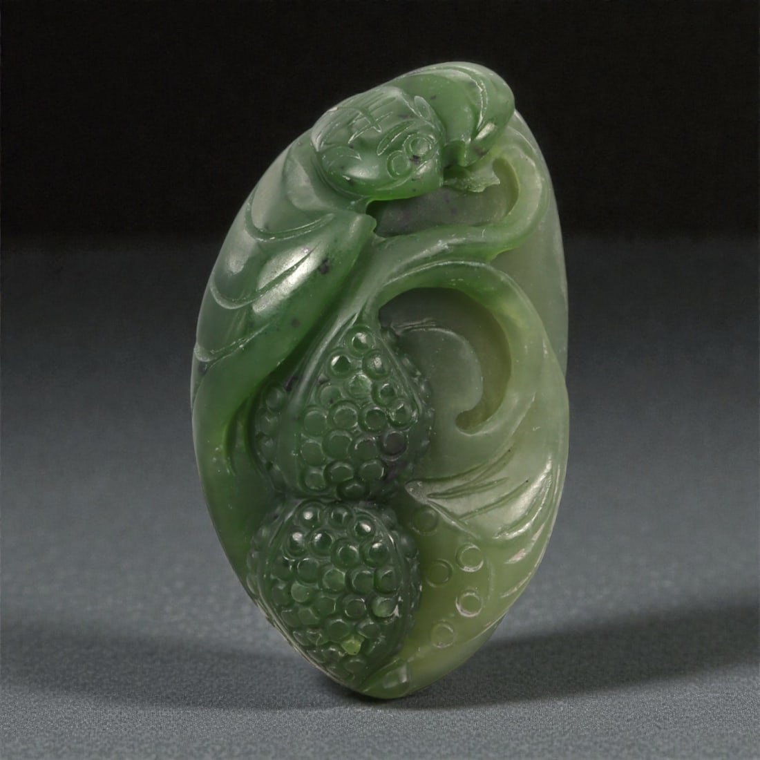 A Chinese Nephrite Jade Bat-and-Fruit Relief Plaque, 20th Century, 40YA: Carved from translucent green nephrite jade with areas of darker saturation and minor natural inclusions, the plaque is worked in relief on one face with a bat shown in association with fruiting forms