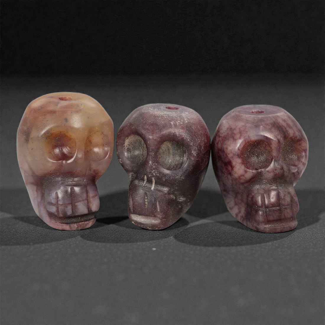 A Group of Tibetan Skull Beads, 20th Century, 42FN: Comprising three beads, each is carved in the form of a human skull with a vertical central perforation for suspension. The surfaces exhibit pronounced natural color variation across the group, rangin