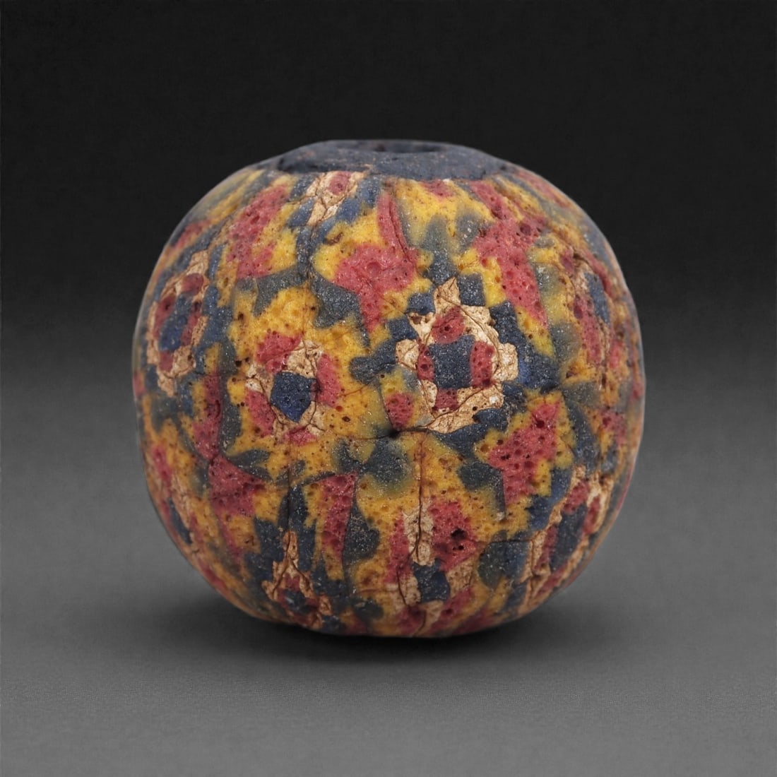 Ancient Glass Bead - Roman Mosaic Cane Sphere, 83J: Formed from multicolored mosaic canes in red, blue, yellow, and white, this bead reflects Roman glassworking traditions of the early centuries CE. The canes were sliced and arranged into a dense, irre