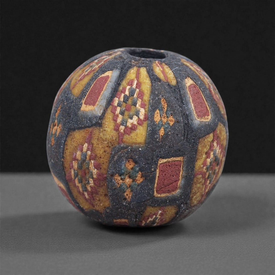 Ancient Glass Bead - Roman Mosaic Panel Sphere, 60J: Formed from alternating mosaic cane panels, this bead illustrates the structured decorative vocabulary of Roman glassworking in the early centuries CE. The patterned canes display small tessellated ar