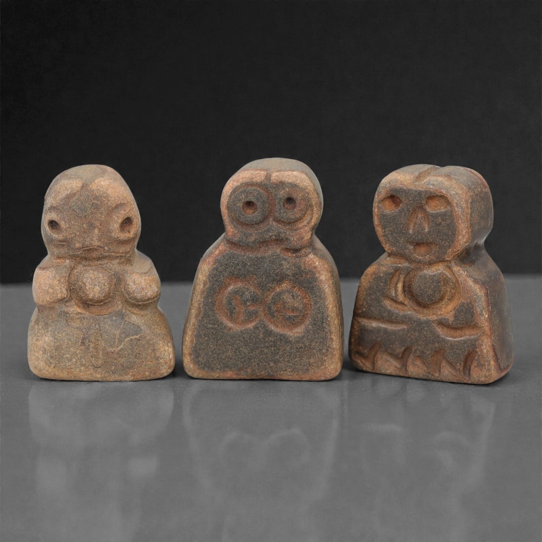 A Group of Three Ancient Near Eastern Stone Idols, 3rd-2nd Millennium BCE, 37FN: Comprising three idols, each is carved from stone with earthy brown and greyish tones, exhibiting natural mineral inclusions and surface patination consistent with age. The leftmost idol is anthropomo