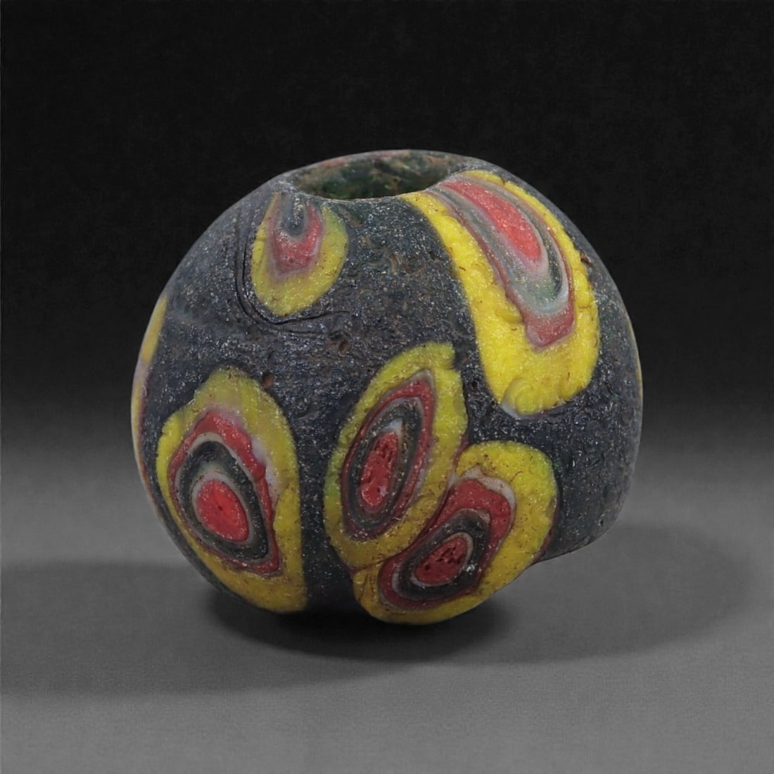 Ancient Glass Bead - Islamic Polychrome Eye-Motif Sphere, 8J: Fashioned in dense multicolored glass, this small spherical bead displays the vivid eye-like motifs associated with Islamic glassworking from the early to mid-first millennium CE. Alternating layers o