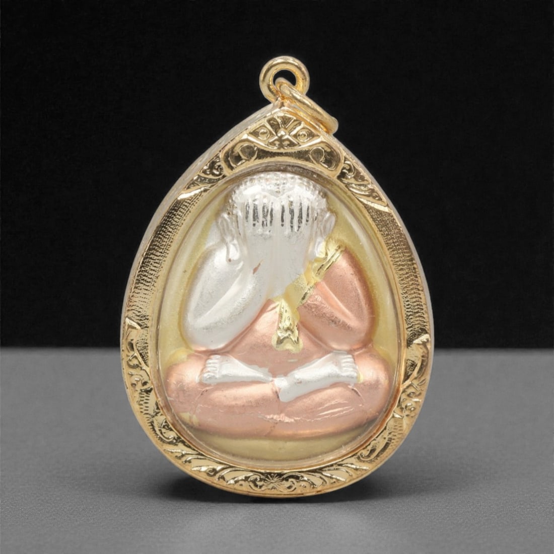 A Thai Phra Pidta Amulet Pendant, 20th Century, 25FP: This teardrop-shaped amulet pendant features the iconic Phra Pidta (Closed-Eye Buddha) figure, encased in an ornate gilded metal frame with a transparent protective cover, measuring 4.6 x 3.3 cm (1 13