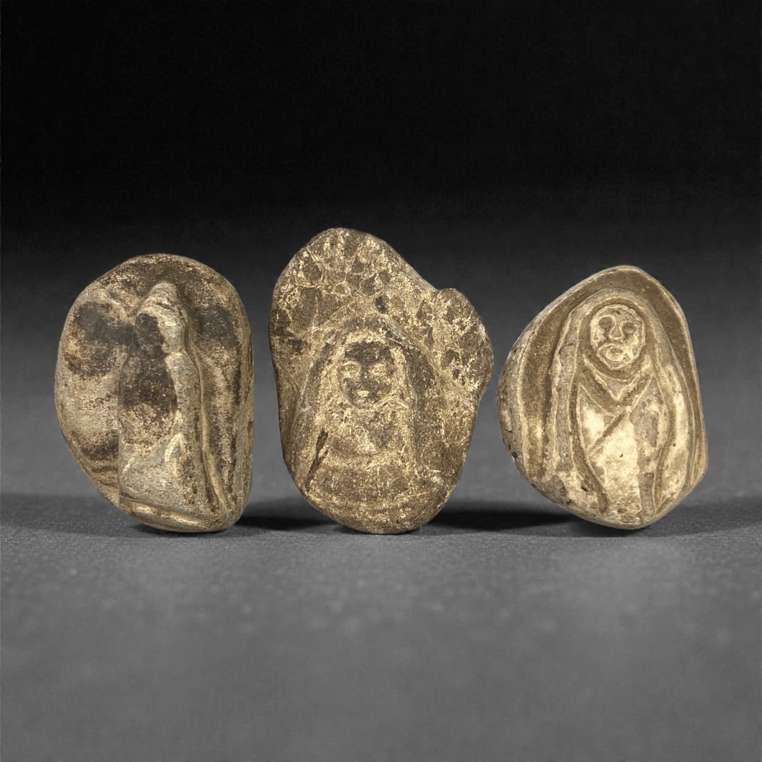 A Group of Three Edo Period Buddhist Stone Carvings, 17th-19th Century, 26FN: Carved from stone with natural tonal variation, surface wear, and mineral encrustation, the three objects depict seated Buddhist figures in shallow relief, each set within an irregular, rounded stone