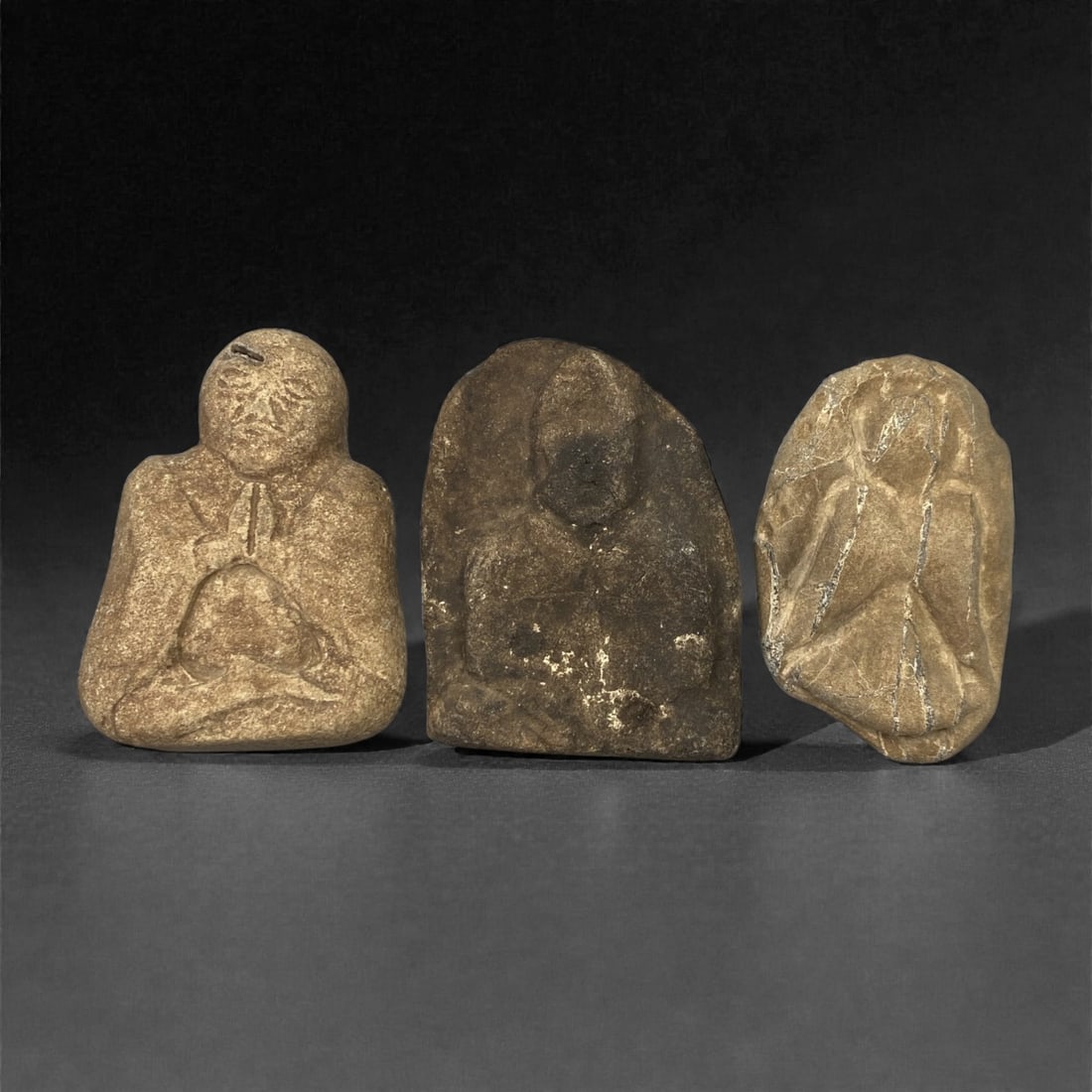 A Group of Three Edo Period Buddhist Stone Carvings, 17th-19th Century, 27FN: Carved from stone with natural tonal variation and surface wear, the three objects depict seated Buddhist figures in a meditative posture. The leftmost figure is rendered in a compact, rounded form, w
