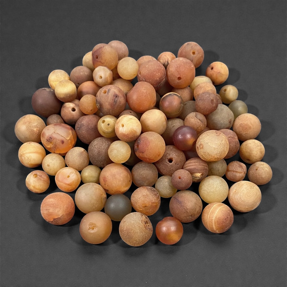 A Tibetan Carnelian Bead Group, 18th-19th Century, 66W, 66W: Comprising approximately ninety-one spherical and near-spherical beads carved from carnelian of varied translucency, the group exhibits a broad range of coloration including pale cream, honey, ochre,