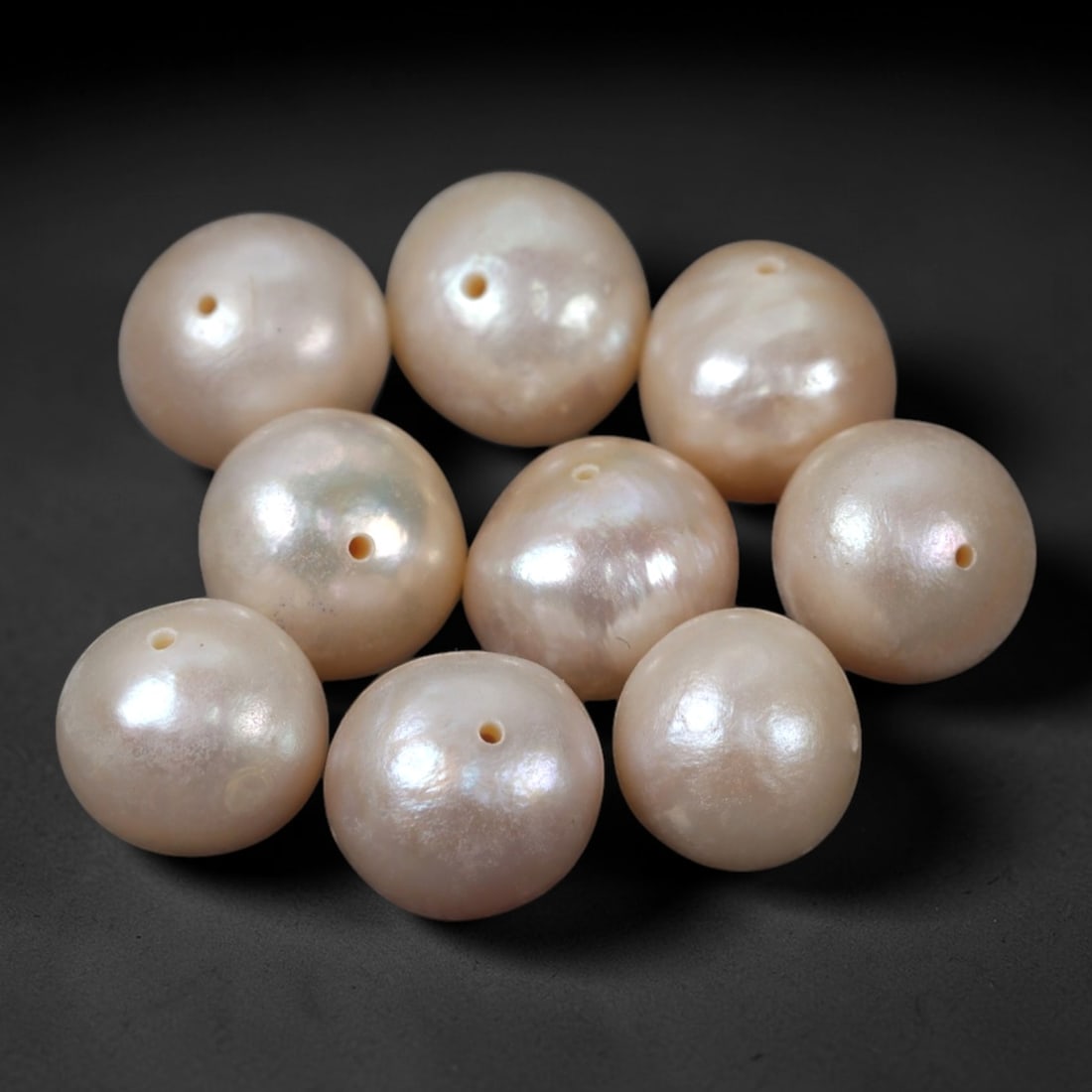 A Group of Nine Baroque Cultured Pearls, 98ZH: Comprising nine baroque cultured pearls, each of spherical to slightly irregular form with a soft pinkish-white hue and subtle iridescent overtones. Each pearl features a small, precisely drilled hole