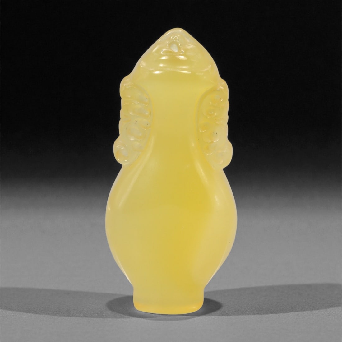 A Chinese Chalcedony Locket Amulet, 20th Century, 94FH: Carved from translucent yellow chalcedony with an even, softly diffused tone, the amulet is formed as a small locket-shaped vessel with a tapering neck and rounded body. The surface is smoothly polish
